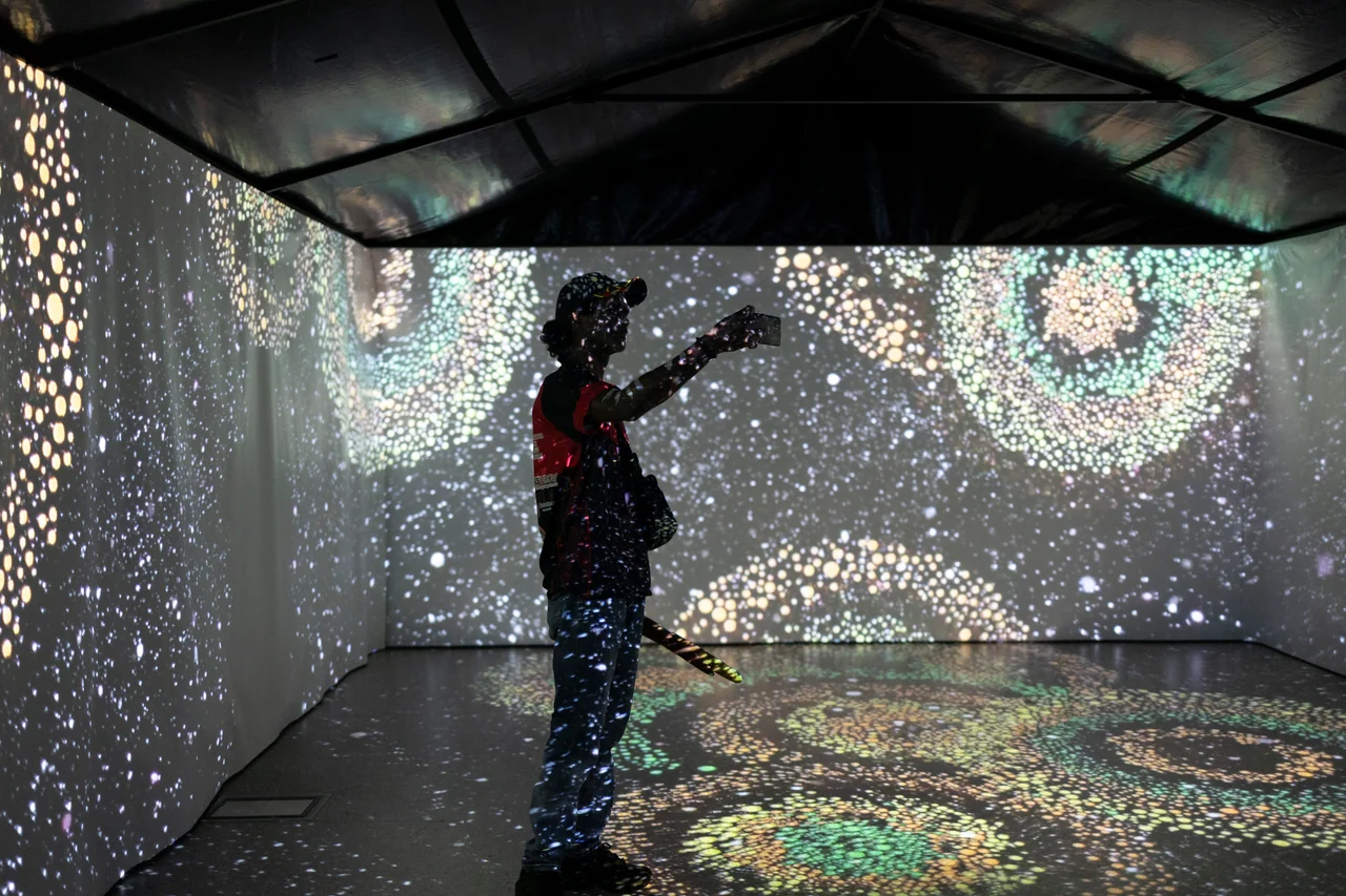 A visitor silhouetted against an immersive projection of shimmering dots in Walking Through a Songline
